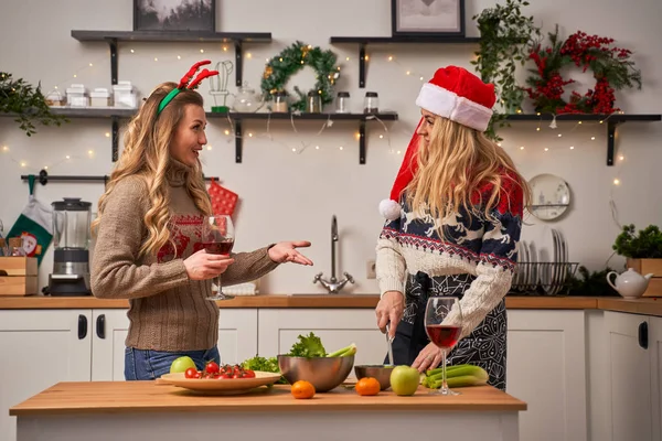 Happy woman with glass and girl cuts celery for New Year in kitchen decorated with Christmas wreaths and garlands — Stockfoto