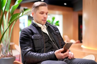 Akıllı telefonlu Brrunet adam yeşil santrale karşı koltukta oturuyor.