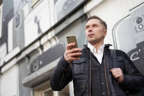 Joven mirando hacia otro lado con el teléfono en las manos a pie en la ciudad — Foto de Stock