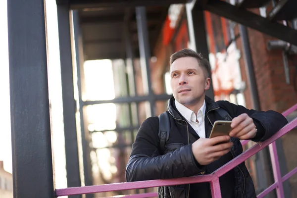 Mężczyzna z telefonem w rękach stojący na fioletowych schodach na tle nowoczesnego budynku — Zdjęcie stockowe