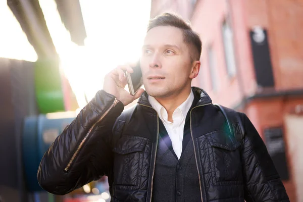 Brunet man talking on phone standing near modern building in afternoon. — Stockfoto