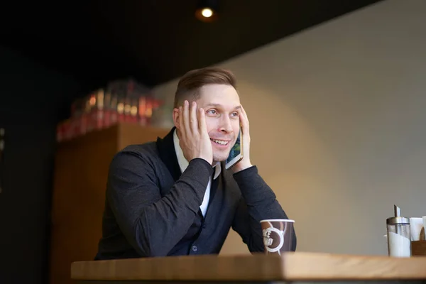 Smiling businessman with phone in hands sitting at table