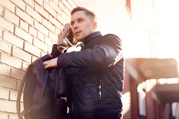 Male looking at side talking on phone while standing by brick modern building on street — Stock Photo, Image