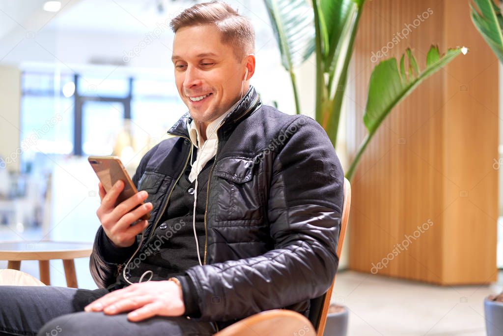 Smiling male with smartphone sitting on chair in store against green plant