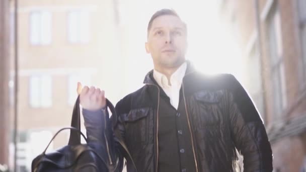 Серьезный мужчина надевает большой черный рюкзак под солнечным светом — стоковое видео