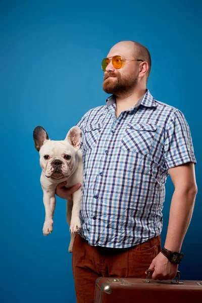 Лысый мужчина с собакой и багажом на пустом синем фоне — стоковое фото