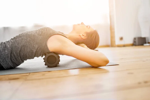 Giovane donna che fa yoga sdraiato sul massaggiatore sul tappeto in palestra durante il giorno — Foto Stock