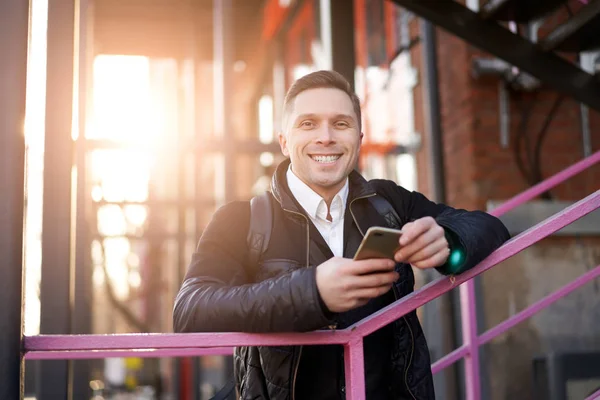 Hombre feliz mirando a la cámara con el teléfono en las manos de pie en las escaleras de color púrpura contra el fondo del edificio moderno — Foto de Stock