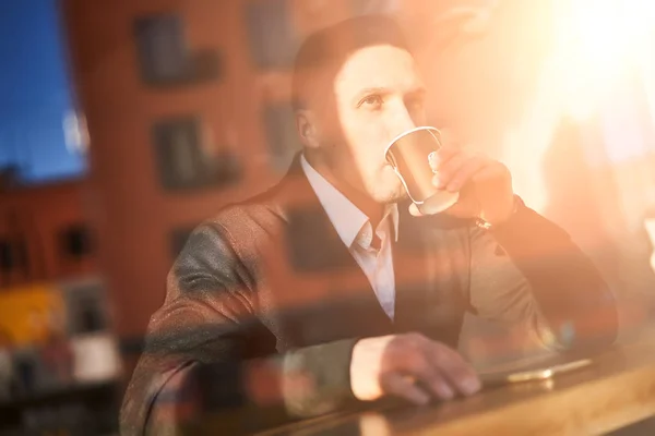 Jovem bebendo de vidro sentado no café, reflexo do edifício — Fotografia de Stock