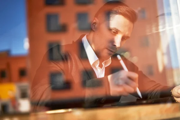 Male businessman with phone and tablet sitting in cafe, building reflection