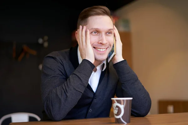 Jovem empresário falando ao telefone enquanto se senta à mesa — Fotografia de Stock