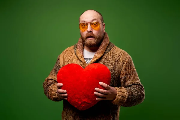 Férfi rózsaszín szemüvegben tartja piros játék szív, miközben áll az üres zöld háttér — Stock Fotó