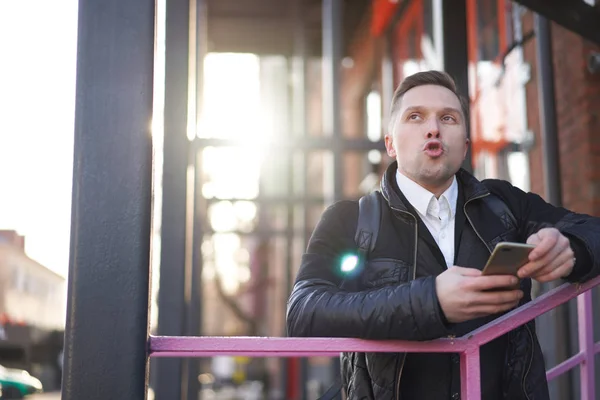 Mężczyzna patrząc na aparat fotograficzny z telefonem w ręku stojący na fioletowych schodach na tle nowoczesnego budynku — Zdjęcie stockowe
