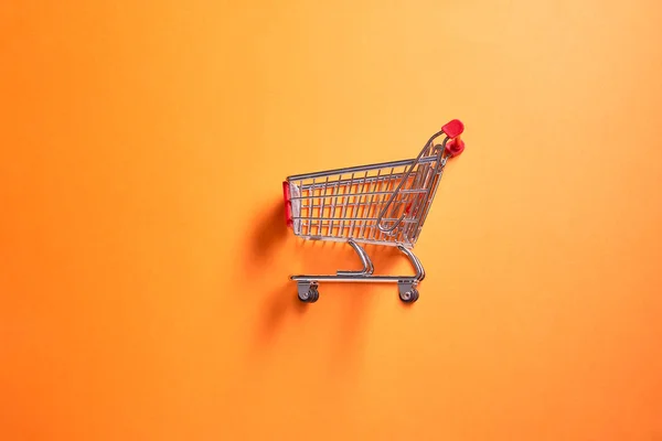 Eiserner Supermarkt-Einkaufswagen auf leerem orangefarbenem Hintergrund — Stockfoto