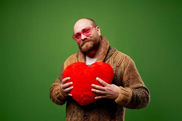 Homme en lunettes orange avec coeur jouet dans ses mains sur fond vert vide — Photo