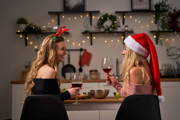 Дві жінки святкують новий рік з келихами для вина в руках, сидячи на кухні . — стокове фото