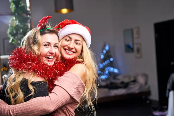 Two hugging women with tinsel during celebration of Christmas in apartment. — 스톡 사진