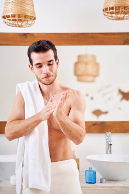 Adam banyo aynasının önünde omuzlarında havluyla dikiliyor.