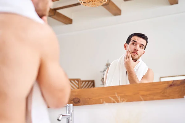 Unshaven naked male with white towel on his neck standing near mirror — Stock Photo, Image