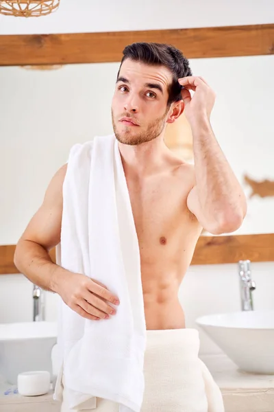 Giovane maschio con asciugamano bianco sulla spalla in piedi da specchio in bagno . — Foto Stock