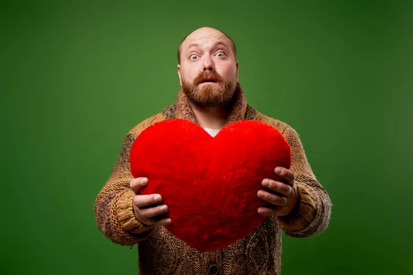 Meglepett férfi kezében játék szív, miközben áll az üres zöld háttér — Stock Fotó