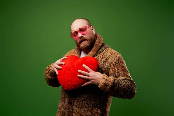 Homme en lunettes orange avec coeur jouet dans ses mains sur fond vert vide — Photo