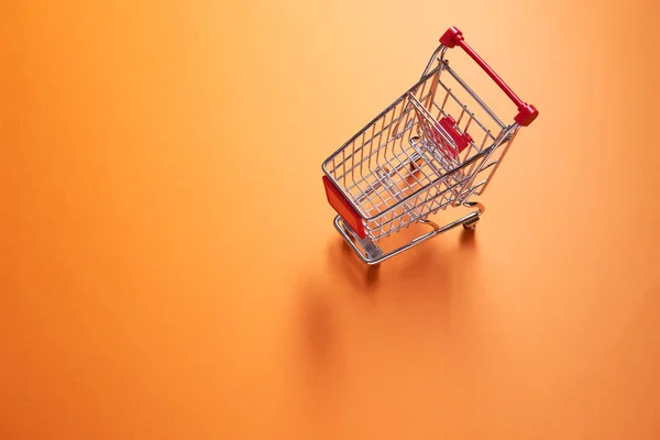 Eisen kleiner Supermarkt-Einkaufswagen auf leerem orangefarbenem Hintergrund — Stockfoto