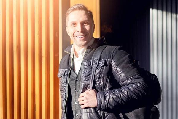 Sonriente hombre de chaqueta se para cerca de la pared de madera en la calle — Foto de Stock