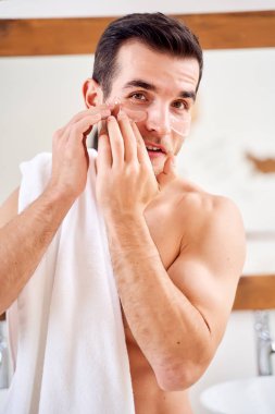 Erkek, banyo aynasında dikilirken gözlerinin altında şeffaf yamalar açar.