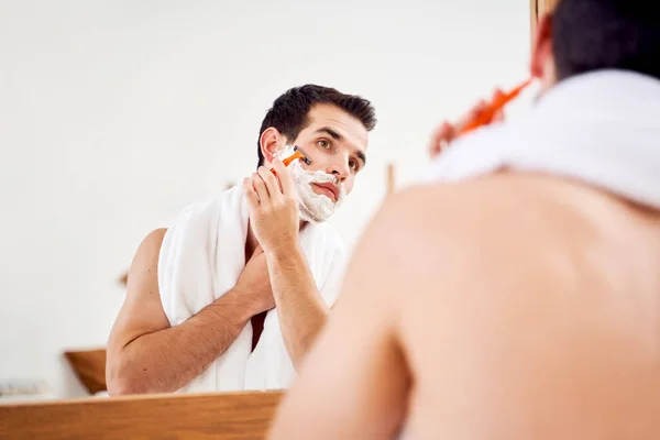 Joven macho con espuma en la barba se afeita cerca del espejo en la mañana —  Fotos de Stock