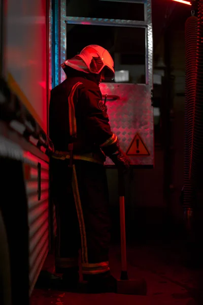 Vollerwerbsfeuerwehrmann mit Hammer auf der Schulter steht neben Feuerwehrauto — Stockfoto