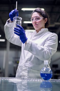 Young lab girl in glasses and white coat with experimental glass in her hands conducts experiments