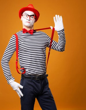 Ciddi pandomimci yelek ve turuncu arka planda izole kırmızı şapkalı kameraya bakıyor.