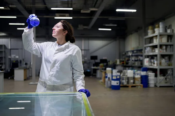 Female lab assistant with flask in hands with blue liquid — Stock Photo, Image