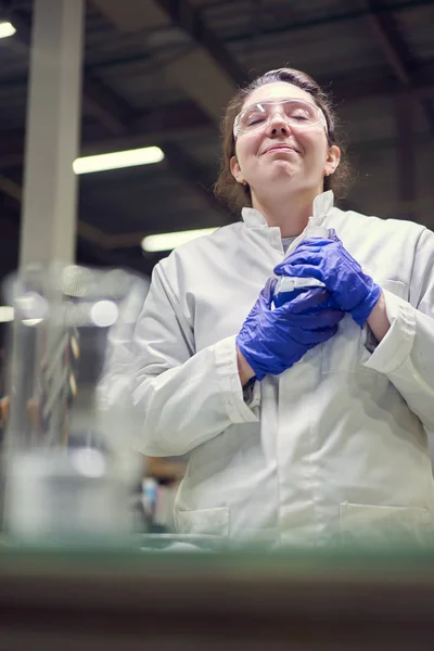 快乐的黑发实验室女性，戴着眼镜，身穿白衣，手里拿着蓝色液体的实验瓶进行实验 — 图库照片