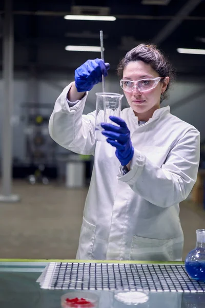 Serious lab woman in glasses and white coat with experimental glass in her hands conducts experiments
