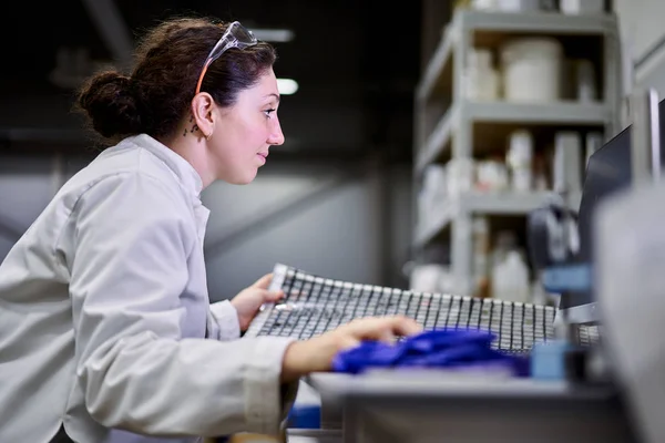 Side view woman in white coat with carbon mesh sits on table in laboratory — Stock Photo, Image