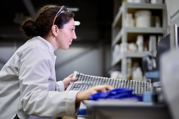 Side view woman in white coat with carbon mesh sits on table in laboratory — Stok fotoğraf