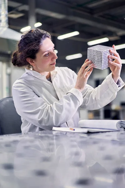 Лаборантка в белом халате с металлическим кубиком сидит на столе в лаборатории — стоковое фото
