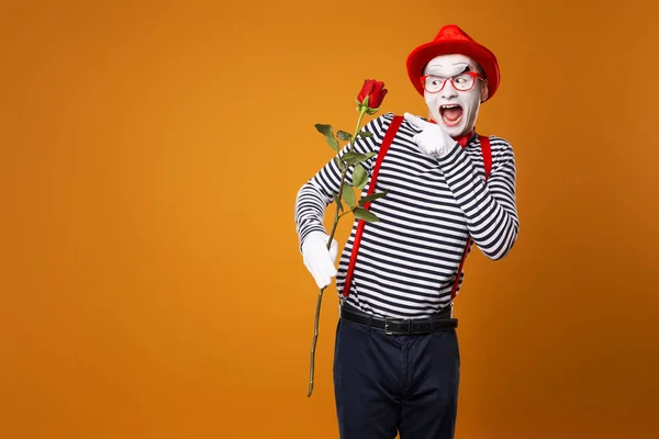 Happy mime met wit gezicht in rode hoed en gestreept t-shirt met roos op lege oranje achtergrond — Stockfoto