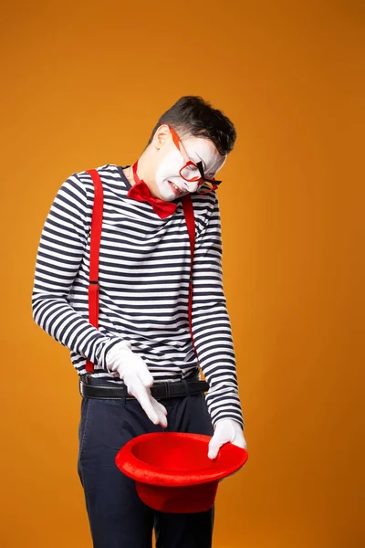 Sorglig mimare i väst håller tom röd hatt på orange bakgrund — Stockfoto
