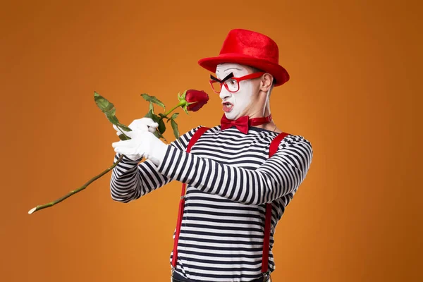 Człowiek mim w czerwonym kapeluszu i kamizelce z różą w dłoniach na pomarańczowym tle — Zdjęcie stockowe