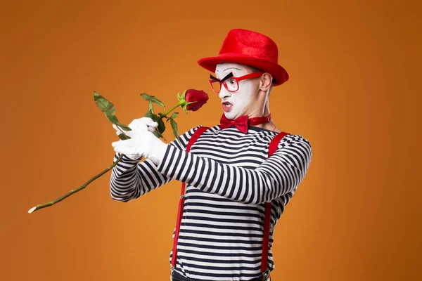 Mime homme en chapeau rouge et gilet avec rose dans les mains sur fond orange — Photo