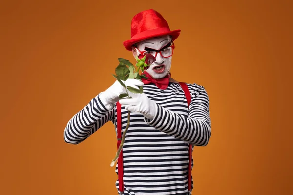 Sério mime homem em chapéu vermelho e colete com rosa nas mãos sobre fundo laranja — Fotografia de Stock