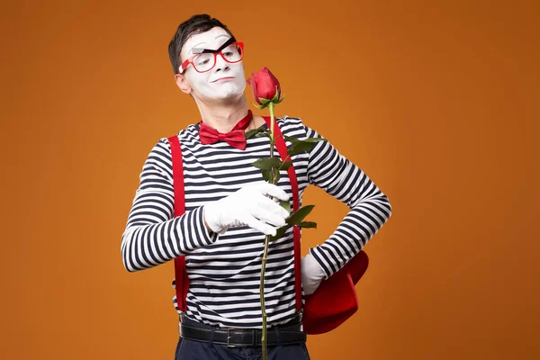 Piros kalapos pantomim, szemüveg és mellény rózsával a kezében narancssárga alapon — Stock Fotó