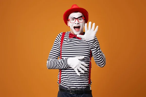 Fröhlicher Pantomime in Weste und rotem Hut auf orangefarbenem Hintergrund — Stockfoto