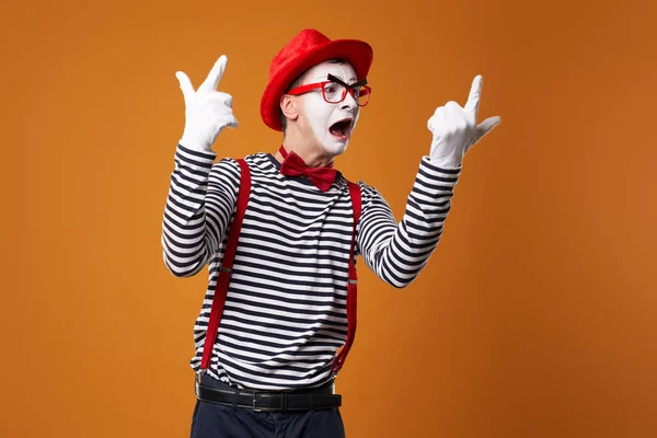 Mime hane i väst och röd hatt med upphöjda handflator tittar på sidan på orange tom bakgrund — Stockfoto