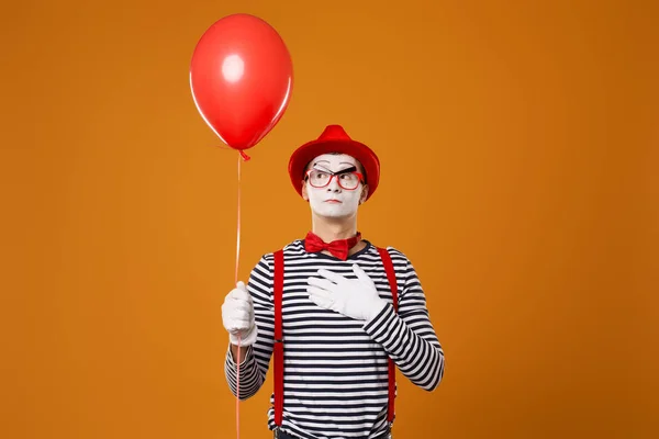 Mime στο γιλέκο και κόκκινο καπέλο με μπαλόνι στο χέρι του σε πορτοκαλί φόντο — Φωτογραφία Αρχείου