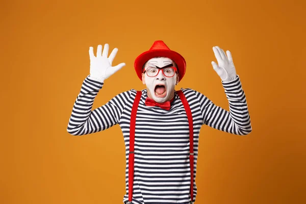 Verrast mime clown in rode hoed en in vest met handen omhoog op oranje achtergrond — Stockfoto