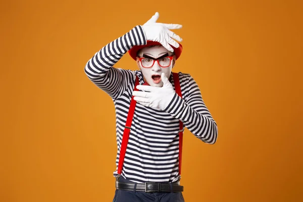 Young mime male in white gloves and red hat on orange background — 스톡 사진
